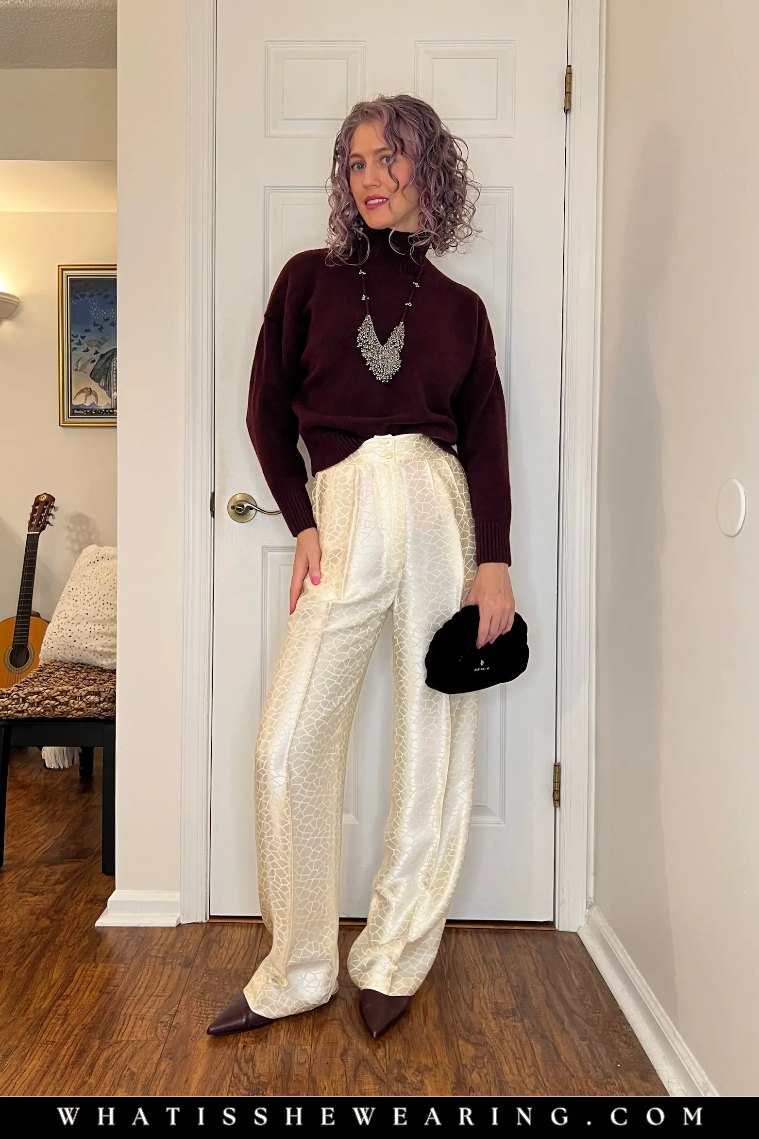 Cozy Sweater Satin Pants Holiday Look Woman in oversized burgundy sweater and ivory wide-leg satin pants for effortless holiday outfit ideas, styled with pointy flats and statement necklace for cozy winter vibes.