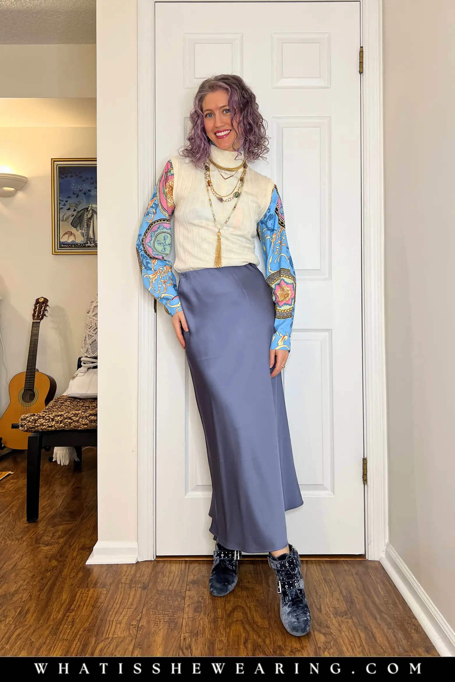 Outfit Idea 3: Bold Patterned Blouse with Vest & Slip Skirt Woman in bold patterned blouse layered under ivory sweater vest, blue satin slip skirt, blue ankle boots, and gold necklace stack for playful business casual